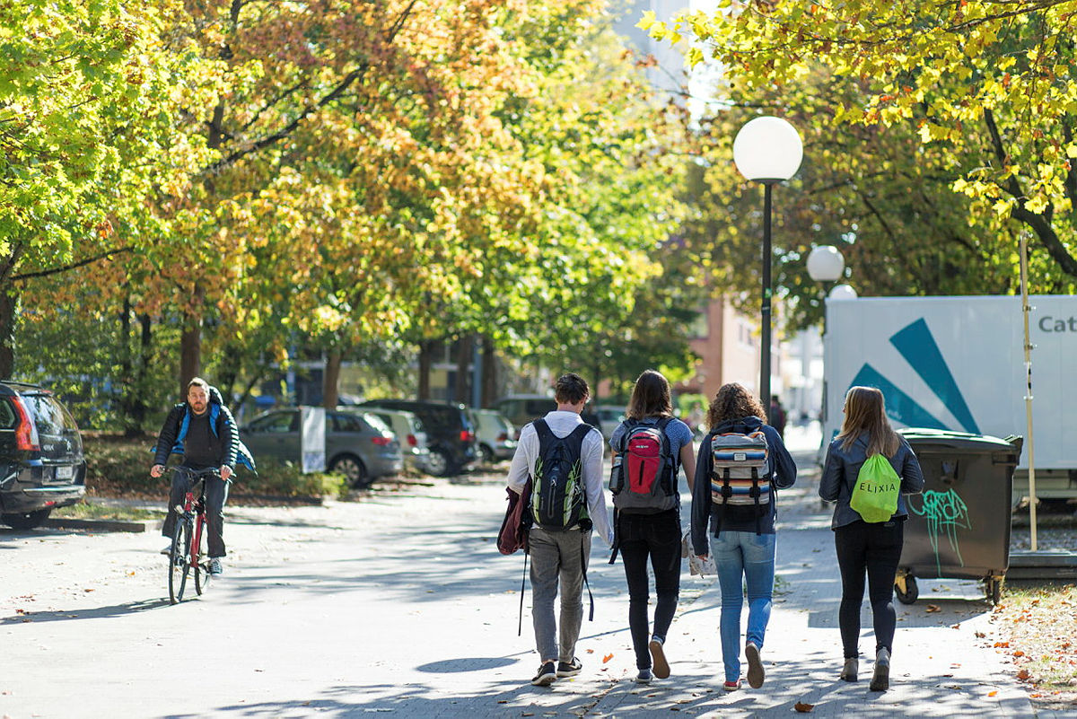 4 Studierende mit Rücksäcken laufen auf den Campus